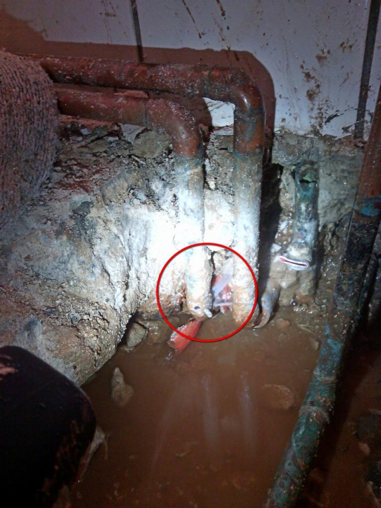 Wyciek wody z uszkodzonej rury, widoczna woda zbierająca się w zagłębieniu, z zaznaczonym czerwonym okręgiem obszarem wycieku.