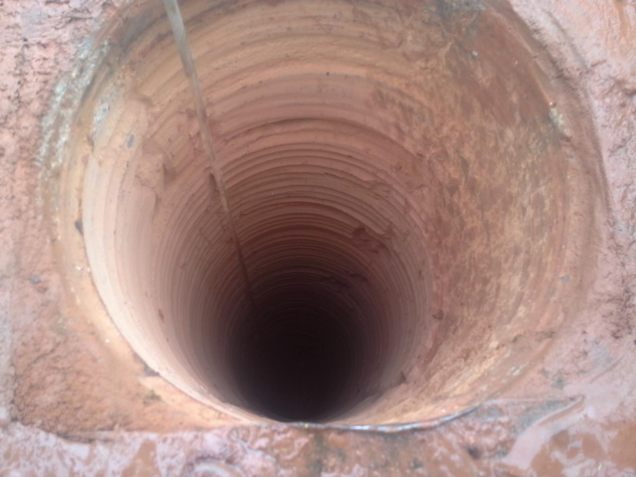 Wnętrze ceramicznego przewodu kominowego z widoczną liną, ujęcie z dołu. Widoczne ślady sadzy i zabrudzeń na ściankach przewodu. Kontrast światła i cienia.