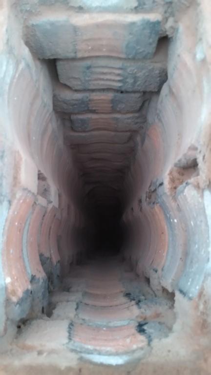 Wnętrze ceramicznego komina z widocznymi spalinami. Ujęcie z dołu, ukazujące konstrukcję i potencjalne osady, co sugeruje potrzebę czyszczenia kominiarskiego.