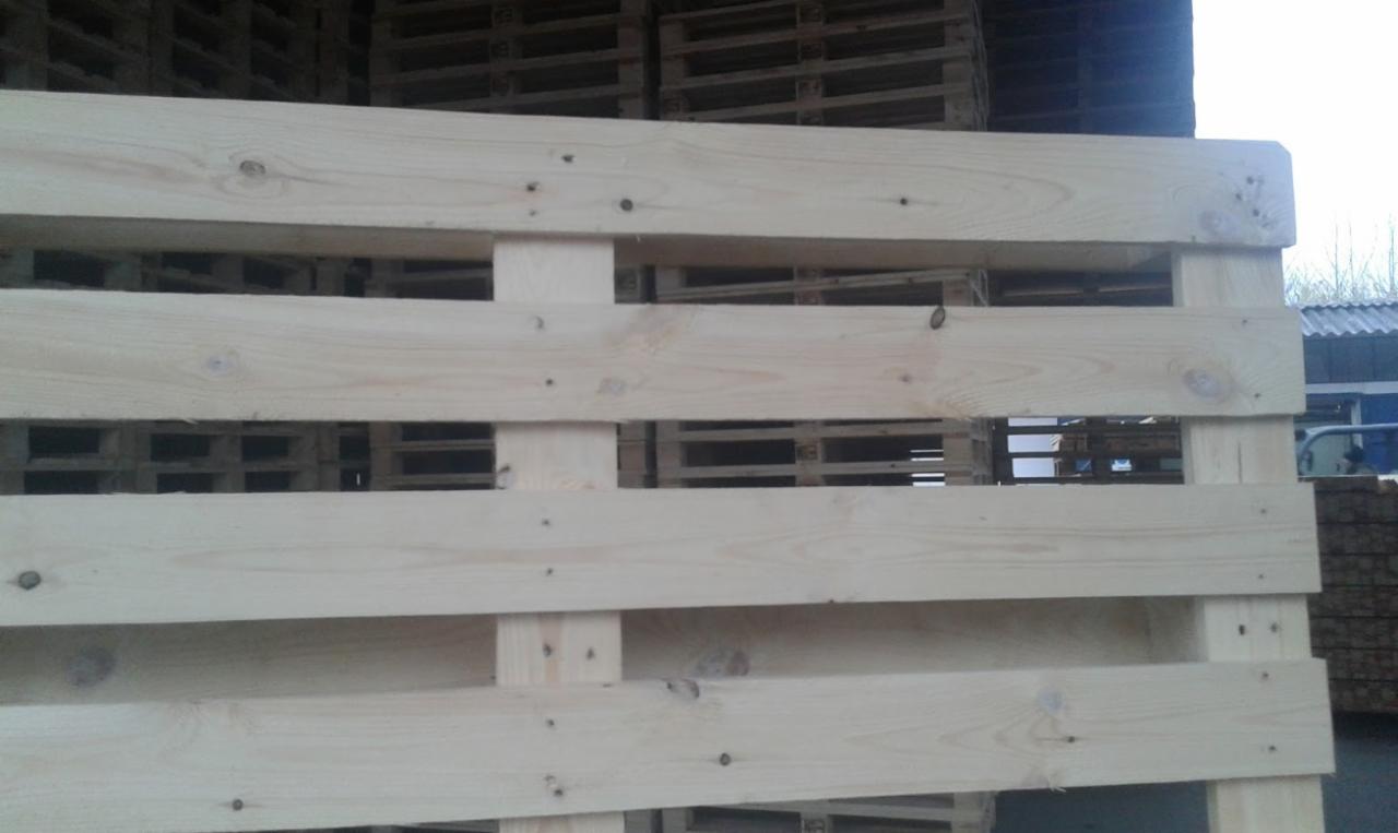 Jasna, drewniana paleta z widocznymi sękami i gwoździami, ustawiona na tle innych palet. Elementy konstrukcyjne wyraźnie zarysowane.