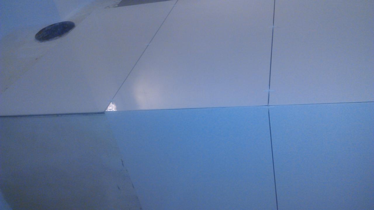 Białe płyty kartonowo-gipsowe, widoczne łączenia i otwór instalacyjny. Jasne, neutralne oświetlenie. Płyty ułożone równo, widoczne delikatne niedoskonałości na powierzchni.