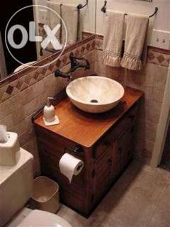 Umywalka nablatowa w kremowym odcieniu na drewnianej szafce w łazience z beżowymi płytkami i lustrem. Widoczne ręczniki i dozownik mydła.