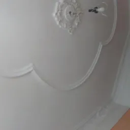 Biały sufit z dekoracyjnym sztukaterią i rozetą pod żyrandol, widoczne niedoskonałości i nierówności powierzchni.