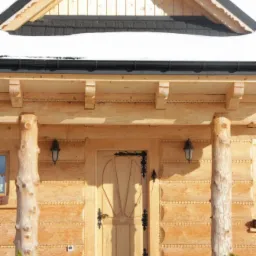 Wejście do jasnego domu z bali, zdobione kolumny z surowego drewna, czarne okucia drzwi i lampy, małe choinki w donicach, śnieg na dachu i przed wejściem.