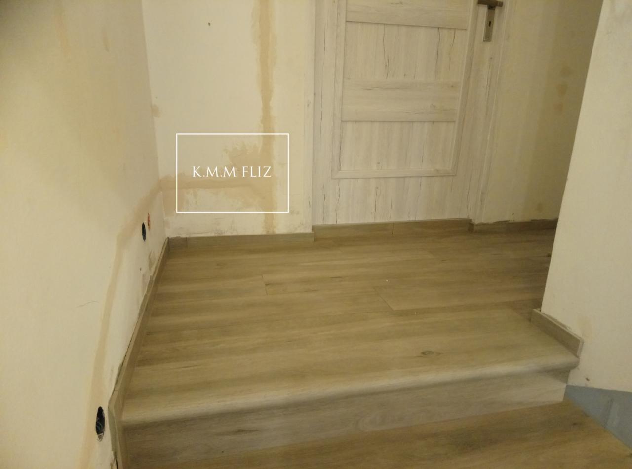 Ułożona jasna podłoga z płytek imitujących drewno, widoczne niedoskonałości ścian przed malowaniem, listwy przypodłogowe dopasowane do koloru podłogi.