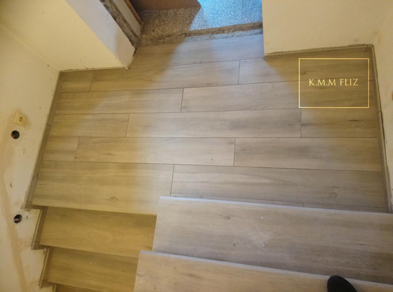 Ułożona podłoga z płytek imitujących drewno na schodach i podłodze, widoczne niedokończone wykończenia ścian i instalacji elektrycznej.