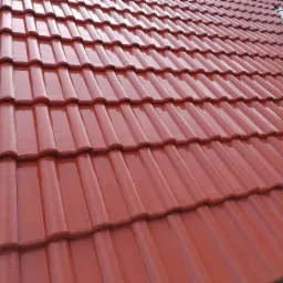 Błyszczący, nowy dach z czerwonej dachówki ceramicznej, ułożonej pod kątem, z widocznymi detalami faktury i delikatnym połyskiem.