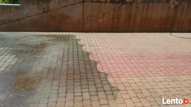 Częściowo umyta kostka brukowa, widoczna różnica w kolorze i czystości między obszarem po lewej stronie, który jest mokry i ciemny, a suchym, jaśniejszym obszarem po prawej stronie, z szarą ścianą...