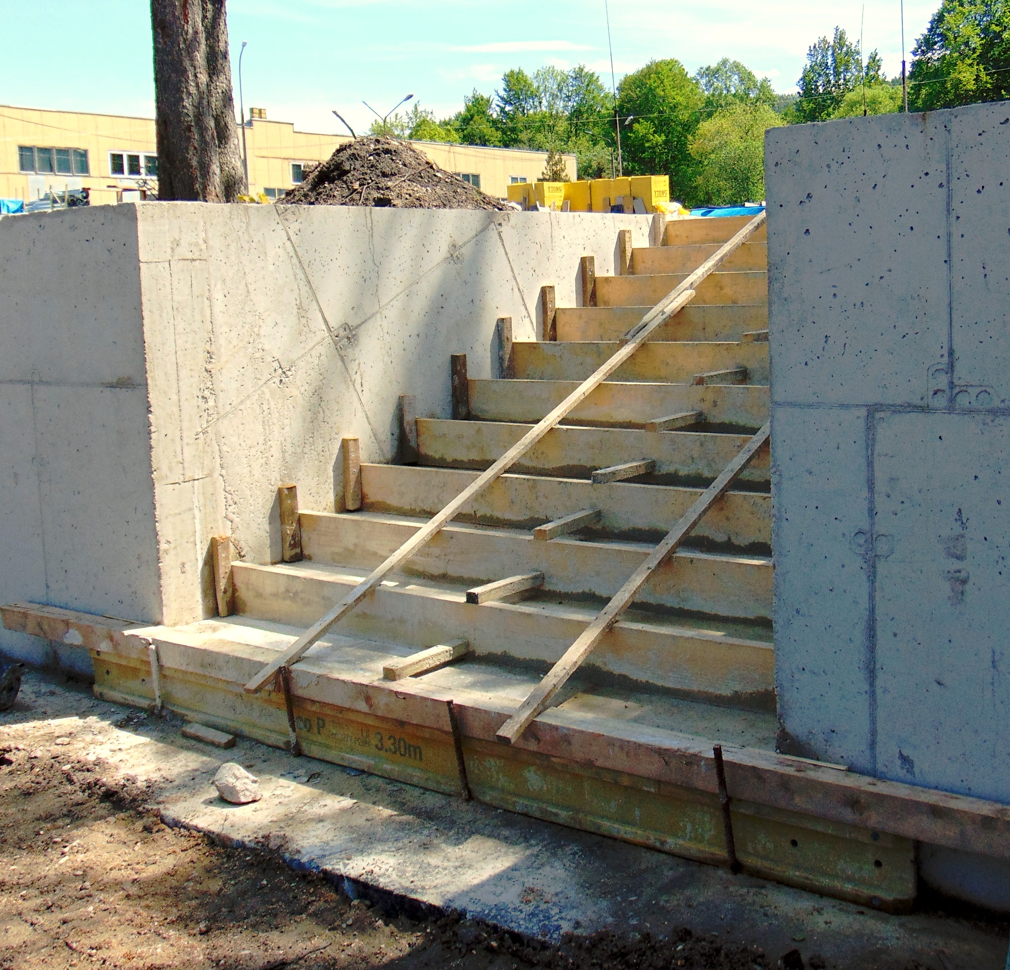 Betonowe schody w trakcie budowy z drewnianym szalunkiem i podporami, widoczne ślady po deskach szalunkowych na betonie.