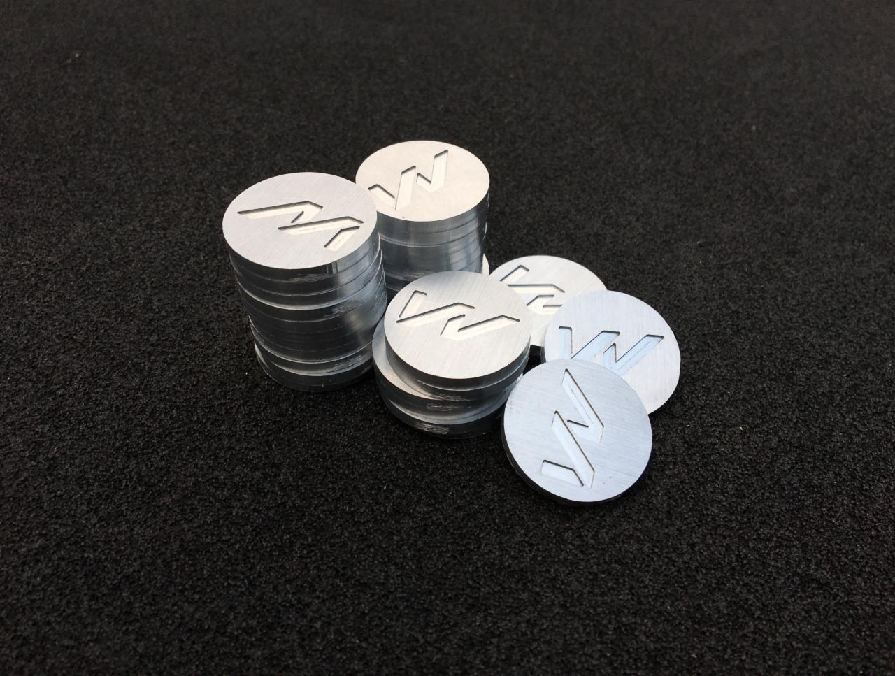Stosy okrągłych, aluminiowych żetonów z wyciętym symbolem na czarnym, teksturowanym tle.