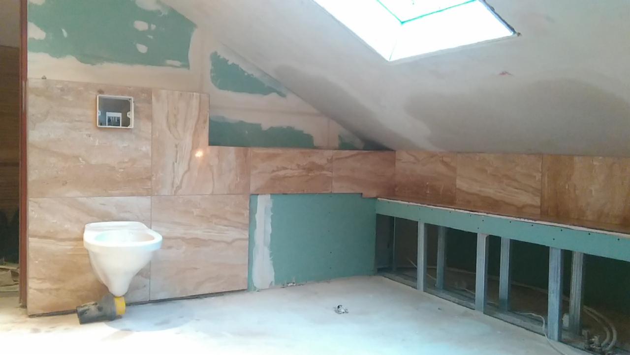 Remont łazienki na poddaszu: częściowo ułożone płytki imitujące marmur, widoczne stelaże pod zabudowę i okno dachowe.