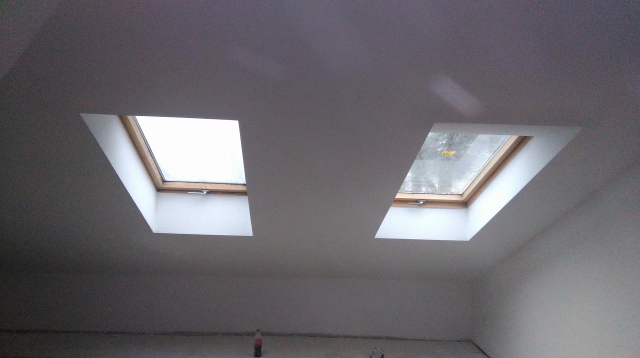 Dwa okna dachowe na poddaszu, widoczne z dołu, po szpachlowaniu i malowaniu. Widoczne gładkie powierzchnie sufitu i ścian w jasnym odcieniu.