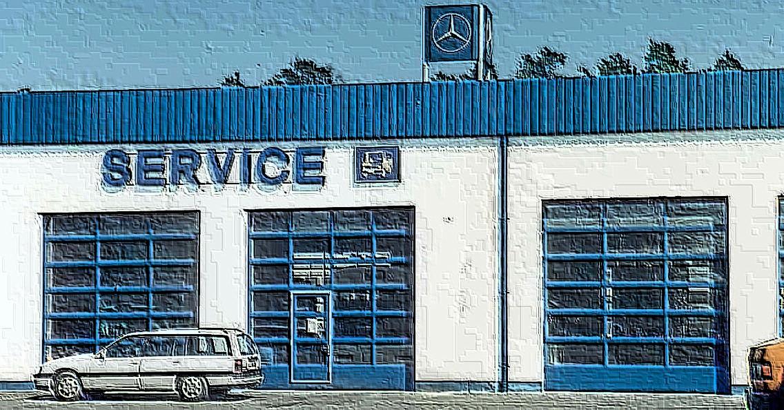 Biało-niebieski budynek serwisu z przeszklonymi bramami garażowymi, logo Mercedes-Benz na dachu i samochodem zaparkowanym przed budynkiem.