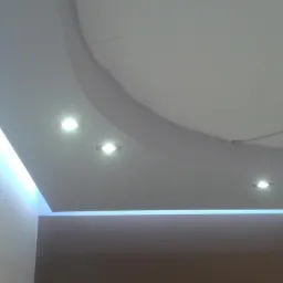 Podwieszany sufit z oświetleniem LED i punktowymi lampami, widok z dołu, nowoczesne wykończenie wnętrza, fragment ściany w tle.