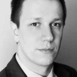 Portret mężczyzny w garniturze i krawacie, czarno-białe zdjęcie z bliska, skupione na twarzy i górnej części ciała.