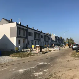 Nowo wybudowane szeregowe domy w Oleśnicy, w trakcie prac wykończeniowych na zewnątrz, widoczni pracownicy budowlani oraz materiały budowlane.