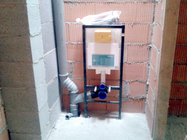 Montaż stelaża podtynkowego WC marki Koło z widoczną instalacją kanalizacyjną w surowym wnętrzu łazienki z ceglanymi ścianami.