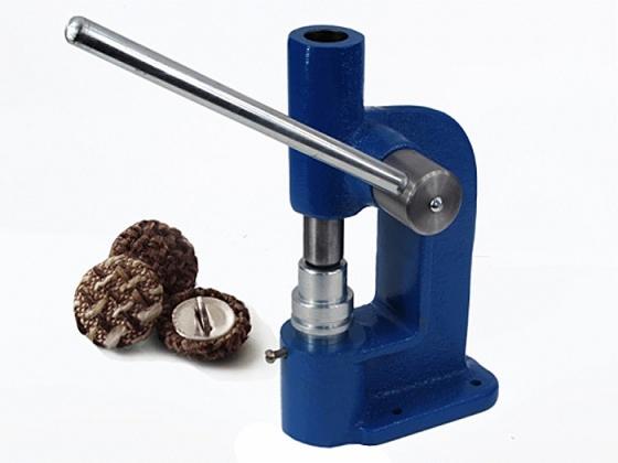 Niebieska prasa ręczna do nabijania guzików tapicerowanych obok trzech guzików, jeden przecięty, ukazujący metalowy rdzeń.