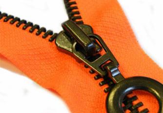 Pomarańczowy materiał z metalowym zamkiem błyskawicznym o dużych ząbkach i okrągłym suwaku, widoczne detale konstrukcyjne.