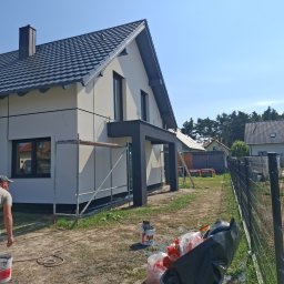 STAN-BUD Radosław Stefański - Nowoczesny dom jednorodzinny w trakcie prac elewacyjnych, widoczne rusztowania, wiadro z farbą i taczka z odpadami budowlanymi na posesji.
