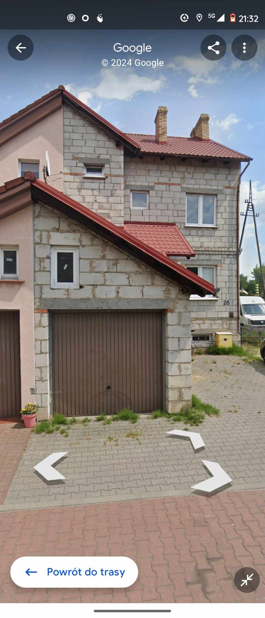 Dwukondygnacyjny dom z garażem, elewacja z białych bloczków, czerwony dach, widok z poziomu ulicy.