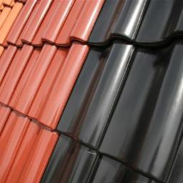 Pokryciadachowenowakowski@gmail.com - Część dachu kryta błyszczącą, czarną dachówką ceramiczną kontrastuje z pomarańczową, tworząc geometryczny wzór. Widok z bliska, z góry pod kątem.