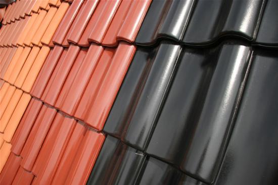 Część dachu kryta błyszczącą, czarną dachówką ceramiczną kontrastuje z pomarańczową, tworząc geometryczny wzór. Widok z bliska, z góry pod kątem.