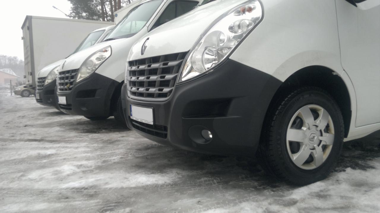 Rząd białych busów Renault Master zaparkowanych na ośnieżonym terenie, widok z niskiego kąta, skupienie na przednich reflektorach i zderzakach.