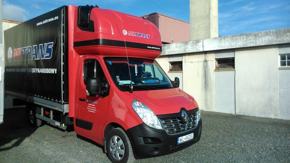 Czerwony bus Renault Master z zabudową kontenerową i logo firmy Miltrans, zaparkowany na tle budynku. Widoczna tablica rejestracyjna, antena CB i detale graficzne na plandece.