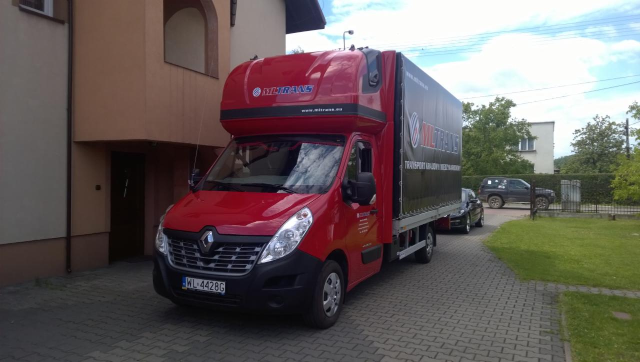 Czerwony bus Renault Master z zabudową kontenerową Miltans, zaparkowany na brukowanej drodze, z logo firmy na nadwoziu i plandece. Widoczny numer rejestracyjny WL 4428G.