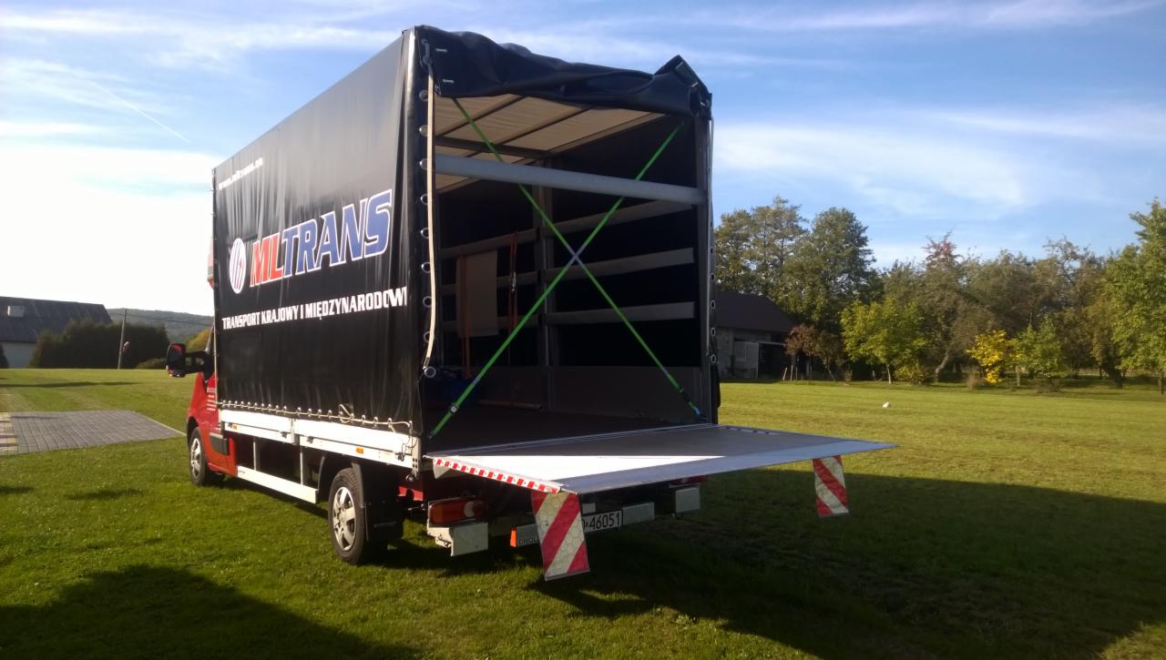 Otwarty, pusty samochód dostawczy z plandeką firmy MLTRANS w Alwerni, gotowy do załadunku. Widoczne zabezpieczenia ładunku i tablica rejestracyjna.