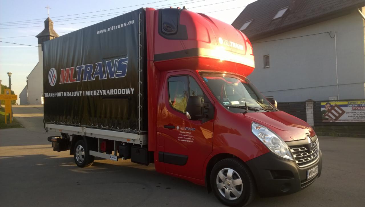 Czerwony bus transportowy MLTRANS z czarną plandeką, zaparkowany na ulicy. Widoczny kościół w tle. Na plandece logo firmy i adres strony www.