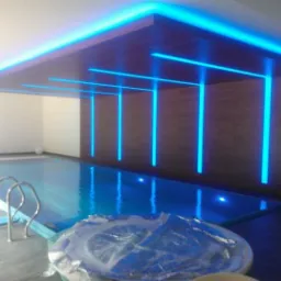 Kryty basen z podświetlanym sufitem i ścianą w stylu minimalistycznym, z liniowymi lampami LED w kolorze niebieskim, odbijającymi się w tafli wody.