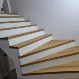 Bieg schodów z drewnianymi stopniami o jasnym odcieniu i białymi podstopnicami, widok z dołu, minimalistyczny design.