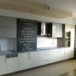 Nowoczesna zabudowa kuchenna w odcieniach bieli i szarości, z tablicą z przepisem na ścianie, oświetleniem punktowym i drewnianymi akcentami.