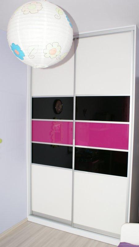 Biała szafa przesuwna z czarnymi i różowymi pasami szkła, oświetlona lampionem z motywem kwiatowym w pokoju dziecięcym.