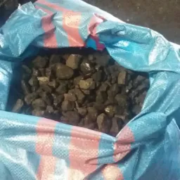 Worek z niebiesko-czerwonymi pasami wypełniony bryłkami węgla. Widoczne błyszczące fragmenty na powierzchni kamieni.