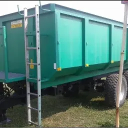 Zielony kontener na gruz z drabinką i platformą, stojący na trawie, widok z boku.