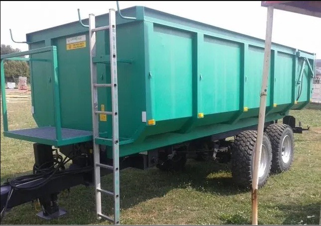 Zielony kontener na gruz z drabinką i platformą, stojący na trawie, widok z boku.