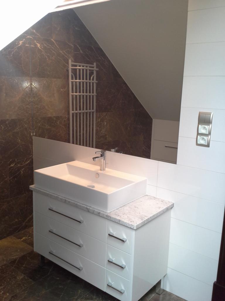 Nowoczesna łazienka: biała szafka z umywalką nablatową i marmurowym blatem na tle brązowych płytek imitujących marmur. Widoczny grzejnik drabinkowy i biała ściana.