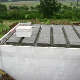 Wznoszenie ścian domu z białych bloczków, widok na strop Teriva z żebrami i podciągami. W tle zieleń pól i lasów.