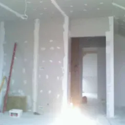 Poddasze w trakcie wykańczania płytami kartonowo-gipsowymi, widoczne szpachlowane łączenia, drabina, poziomica i materiały izolacyjne.