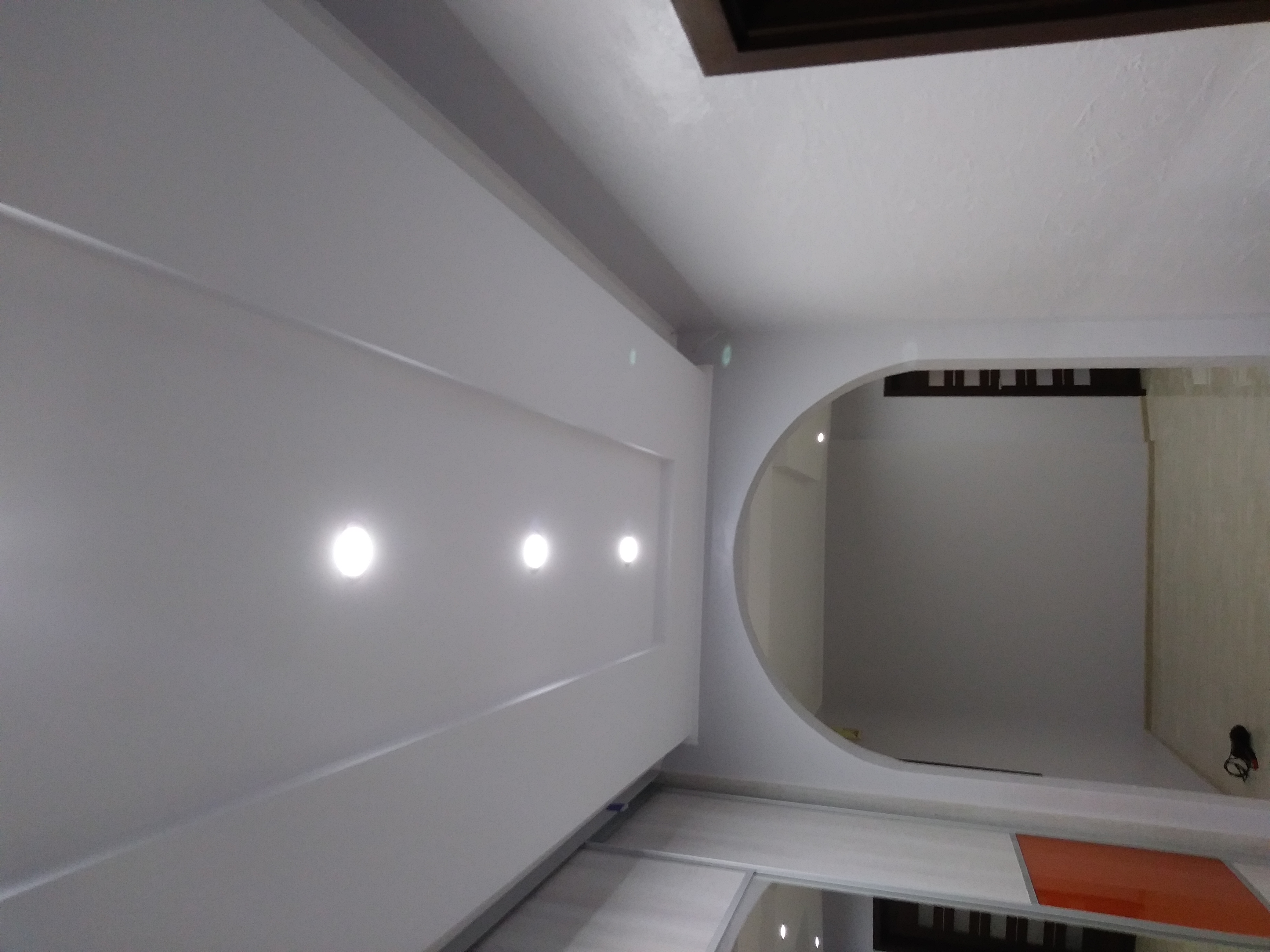 Nowoczesny sufit podwieszany z oświetleniem punktowym i łukowatym przejściem do innego pomieszczenia, widok z dołu.