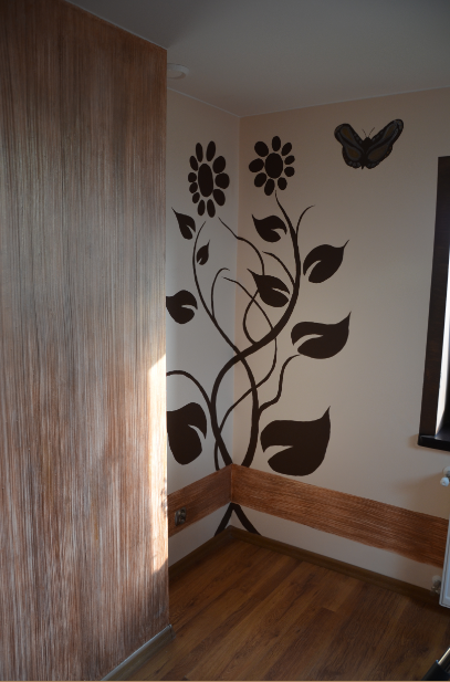 Wnętrze pokoju z dekoracyjną ścianą imitującą drewno i naklejkami ściennymi przedstawiającymi kwiaty i motyla, drewniane listwy przypodłogowe.