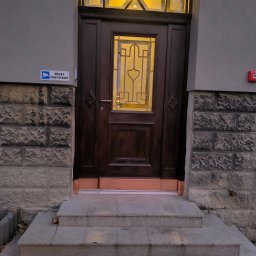 Olaf Wiewióra AWO SERWIS - Ciemne, drewniane drzwi wejściowe z szybą i ozdobnymi elementami, oświetlone od wewnątrz, z numerem 15 na ścianie i schodami prowadzącymi do wejścia.