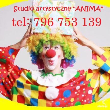 Klaun w kolorowym stroju i peruce, z czerwonym nosem, trzymający na głowie prezent z napisem 'Studio artystyczne ANIMA' i numerem telefonu.