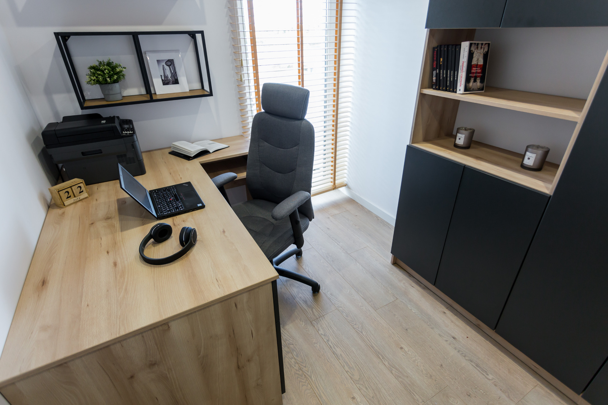 Nowoczesny gabinet w domu: biurko z laptopem, słuchawkami i kalendarzem, ergonomiczne krzesło, regał z książkami i dekoracjami.