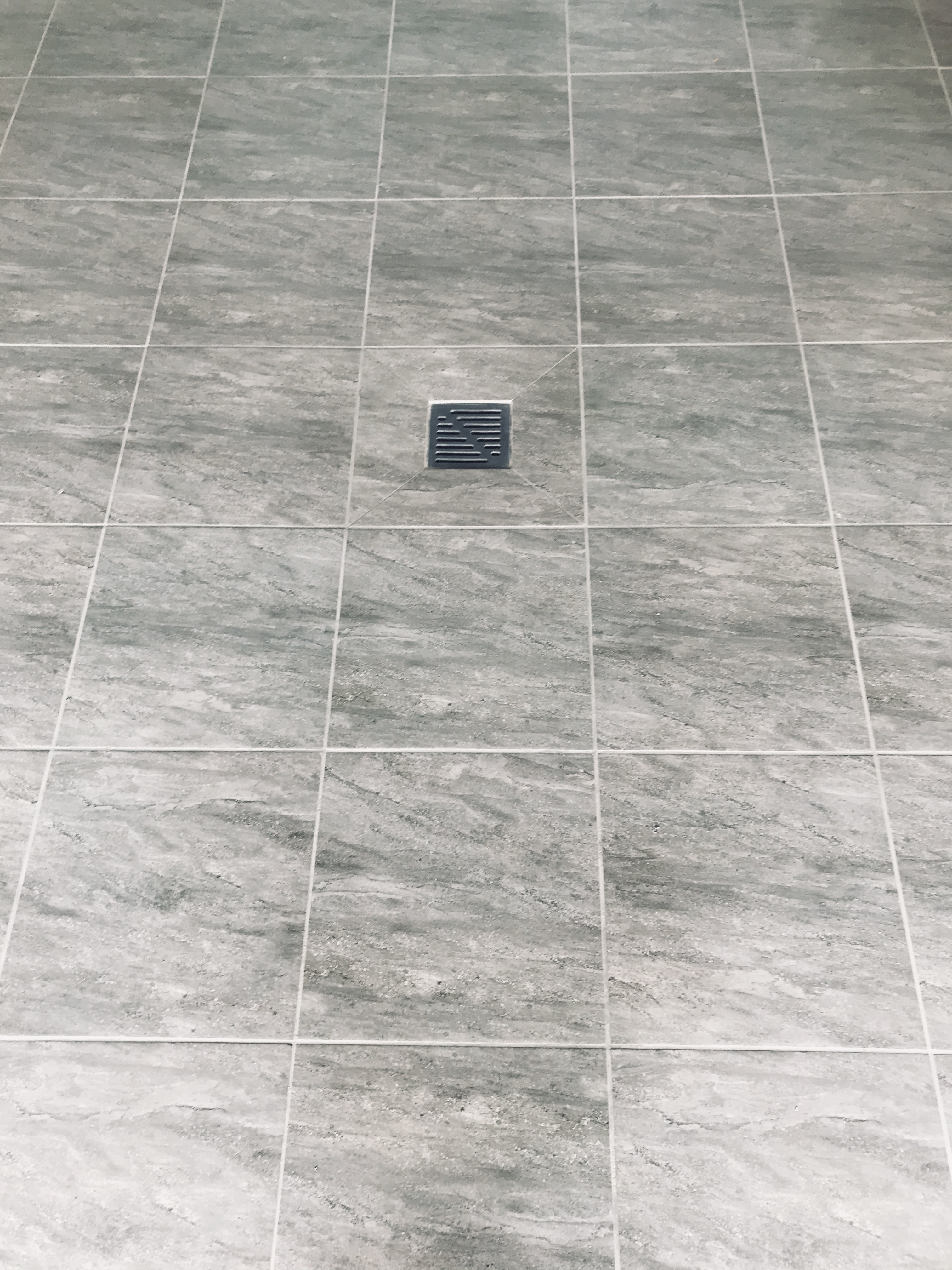 Szare, kwadratowe płytki podłogowe z odpływem liniowym pośrodku, widok z góry.