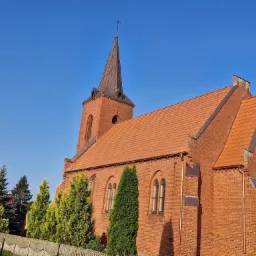 Ceglany kościół z czerwoną dachówką i miedzianymi rynnami w Pile, widziany z dołu. Na drabinie osoba przy oknie. Wieża z krzyżem.