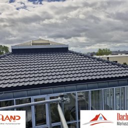 DACH-MAR Mariusz Adamczewski - Czarny dach z dachówki ceramicznej z lukarną, widok z góry na tle pochmurnego nieba. Fragment rusztowania i okien budynku w dolnej części kadru.